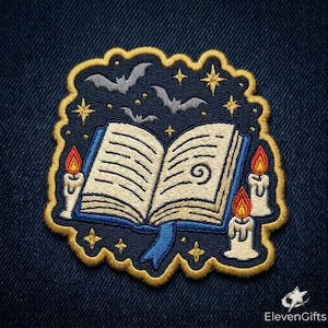 May include: An embroidered patch featuring an open book with cream pages and blue covers, surrounded by three lit candles with orange and yellow flames, three grey bats, and gold stars against a dark blue background with a gold border.