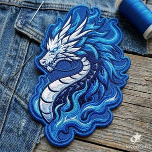 May include: An embroidered patch featuring a stylized dragon head and neck in shades of white, light blue, and dark blue. The dragon is surrounded by swirling flame-like patterns in various blue tones, creating a dynamic and detailed design.