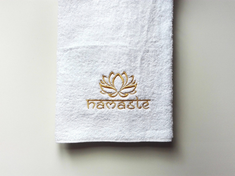 May include: White bath towel with gold embroidery of a lotus flower and the word "namaste".