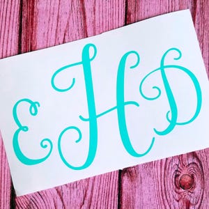 May include: A white rectangular sheet featuring the teal-colored letters E, H, and D in a decorative, cursive script font. The letters are arranged horizontally across the center of the white surface, showcasing a smooth, matte finish.