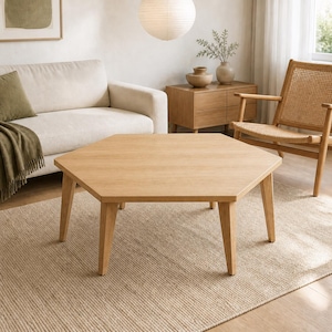 May include: A light-toned wooden coffee table with a hexagonal tabletop and six tapered legs. The table features a smooth, flat surface with a visible wood grain pattern, providing a stable base for living room use in a neutral-coloured space.