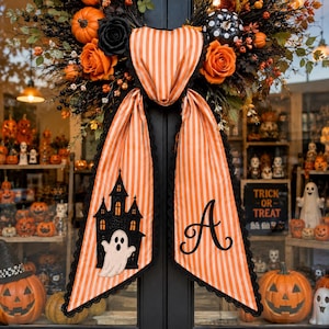 May include: A Halloween wreath featuring orange and black striped fabric ribbons, one side displaying a black haunted house silhouette with a white ghost, the other side featuring a black embroidered letter A, accented with orange roses and pumpkins.