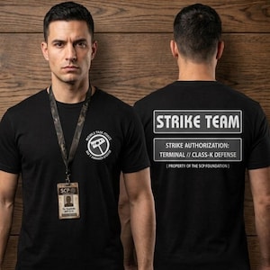 Könnte beinhalten: Ein schwarzes T-Shirt mit einem weißen kreisförmigen Logo auf der Brust mit dem Text "MOBILE TASK FORCE" und "NO. 7 HAMMER DOWN". Die Rückseite zeigt den weißen Text "STRIKE TEAM", "STRIKE AUTHORIZATION: TERMINAL // CLASS-K DEFENSE" und "[ PROPERTY OF THE SCP FOUNDATION ]".
