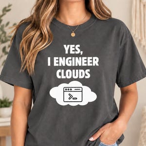 May include: A charcoal gray short-sleeve t-shirt featuring the white text "YES, I ENGINEER CLOUDS" above a white cloud graphic containing a black computer terminal icon with a command prompt symbol inside the browser window frame.