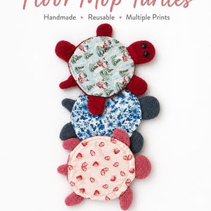 May include: Three turtle-shaped floor mop covers stacked vertically. The top turtle is red with a light blue winter-themed shell. The middle turtle is dark gray with a blue floral shell. The bottom turtle is pink with a light pink strawberry shell.