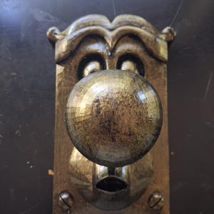 May include: A brass-toned door knob set featuring a spherical knob mounted on a rectangular backplate. The metal surface has a distressed, antiqued finish with visible dark patina. Two screws are visible at the bottom of the plate.