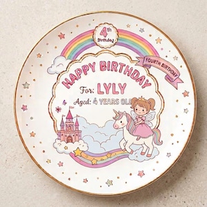 Puede incluir: Un plato redondo de cerámica blanca con borde dorado que presenta una ilustración colorida de un unicornio, una princesa y un castillo sobre nubes. El texto dice Happy Birthday, For: LYLY, Aged: 4 YEARS OLD, 4th Birthday y Fourth Birthday.