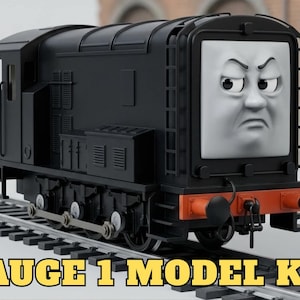 May include: A black diesel locomotive model train featuring a front face with an angry expression, detailed side vents, and a red buffer beam. The train is positioned on a grey track, and the text GAUGE 1 MODEL KIT is displayed at the bottom.