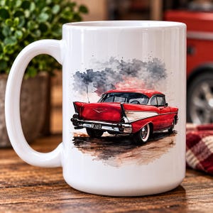 May include: A white ceramic mug featuring a watercolour-style illustration of a red 1957 Chevrolet Bel Air seen from the rear. The classic car has chrome bumpers, white-wall tyres, and a number plate reading 1957 against a soft, abstract background.