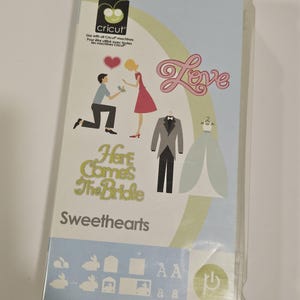 May include: A Cricut Shapes Cartridge case titled Sweethearts featuring illustrations of a couple, a wedding dress, a tuxedo, the word Love, and the text Here Comes The Bride. The packaging includes icons of rabbits, shapes, and uppercase and lowercase letters.