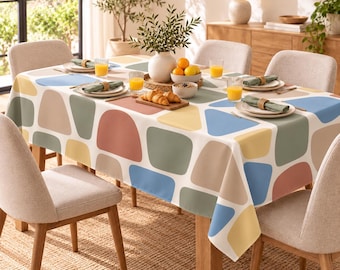 Peut inclure: Une nappe rectangulaire ornée d'un motif répétitif de formes géométriques arrondies dans des tons sourds de bleu, jaune, vert sauge et terre cuite sur fond blanc, recouvrant une table à manger en bois avec quatre chaises beige clair.