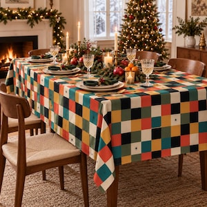 May include: A rectangular tablecloth featuring a multi-colored checkered pattern in shades of red, yellow, teal, and black, accented with small star motifs. The fabric drapes over a dining table set with white plates, glassware, and candles.
