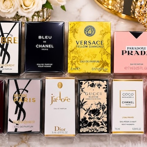 Può includere: Una collezione di dodici scatole di profumo in miniatura di vari marchi di lusso tra cui Yves Saint Laurent, Chanel, Versace, Prada, Tom Ford, Dior, Gucci e Giorgio Armani, disposte in due file su una superficie di marmo con testo visibile.