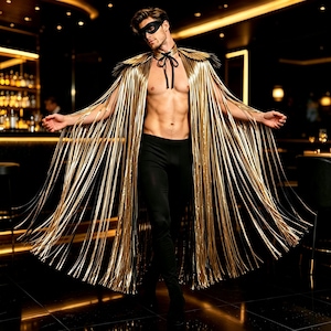 May include: A metallic gold fringe cape featuring a high collar with a black ribbon tie closure. The cape is worn over black leggings and paired with a black eye mask. The long, thin gold strips create a dramatic, flowing effect that extends from the shoulders down to the floor, covering the arms and torso.