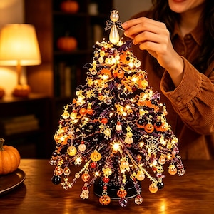 May include: A tabletop artificial tree with dark purple branches decorated with miniature orange pumpkin ornaments, spider webs, and glowing warm white fairy lights. A white pearl-like angel topper sits at the peak of the tree.