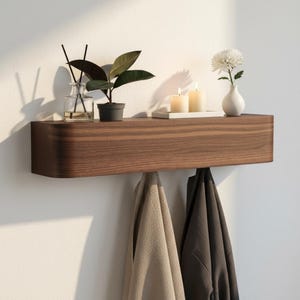 Puede incluir: Un estante flotante montado en la pared hecho de madera marrón oscura con bordes redondeados. La superficie superior sostiene un difusor de varillas de vidrio, una pequeña planta en maceta, dos velas blancas en una bandeja y un florero.