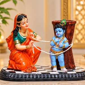May include: A decorative figurine depicting a woman in an orange and green sari kneeling while tying a white rope around a blue-skinned child standing next to a brown wooden pillar. The figures are set on a black and white checkered oval base.