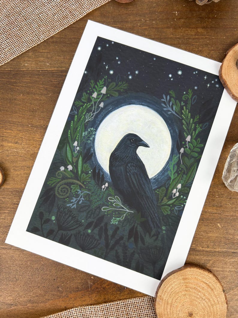 Peut inclure: Une impression d'art encadr&eacute;e repr&eacute;sentant un corbeau noir devant une pleine lune. Le corbeau est entour&eacute; d'un feuillage vert fonc&eacute;, de champignons blancs et d'&eacute;toiles sur un fond bleu fonc&eacute;. L'&oelig;uvre est sur fond blanc.