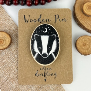 May include: A wooden pin featuring a black and white badger with a crescent moon and stars in the background. The pin is oval shaped and has the text "Wooden Pin" and "alice darkling" on the card.