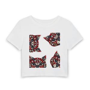May include: A white short-sleeved t-shirt featuring a graphic print of four cat heads arranged in a square formation. Each cat head is composed of intricate geometric patterns in shades of red, black, white, and grey, with visible eyes.