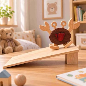 Op de afbeelding: Een houten krabspeelgoed met een donkerbruin ovaal lichaam, lichtbruine scharen en een klein rood schildvormig accent in het midden. De krab staat op een lichtgekleurde houten helling die aan één kant door een blok wordt verhoogd.