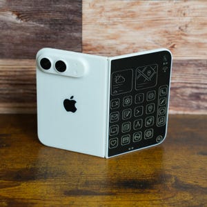 May include: A white foldable smartphone with a black Apple logo on the back and a dual-lens camera module. The interior screen displays a black interface with white line-art icons for weather, maps, phone, messages, and various system applications.