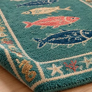 Könnte beinhalten: Ein blaugrüner Teppich mit einem wiederkehrenden Muster aus Fischen in Blau-, Creme- und Korallentönen. Der Teppich hat einen breiten Rand, der mit Seesternen, Seepferdchen und Korallenmotiven in Creme, Beige und Orange verziert ist.