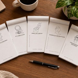 May include: Five white rectangular notepads with black line art illustrations and text. Each notepad features a unique design including a dog, headphones, envelopes, a moon, and a cactus, along with checkboxes and lines for list-making tasks.