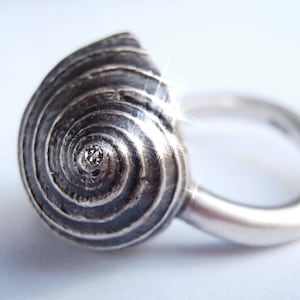May include: A silver ring with a spiral shell design and a small diamond in the center.