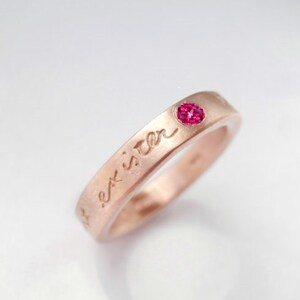 May include: A rose gold ring with the inscription "best sister" and a small pink gemstone.
