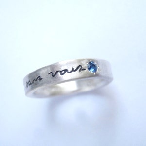 May include: A silver band ring with a blue gemstone and the inscription "Je t'aime" engraved on the band.