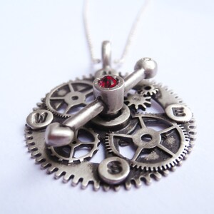 May include: Silver pendant necklace featuring a red gemstone and a design of interlocking gears.