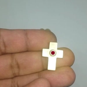 May include: A small gold cross pendant with a red gemstone in the center.