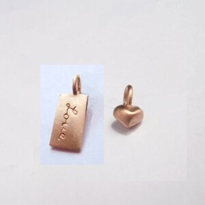 May include: Two gold-toned metal charms. One charm is a rectangular tag with the word "Love" engraved on it. The other charm is a heart shape.