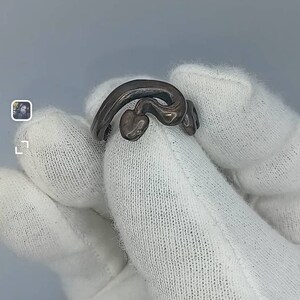 May include: A silver ring shaped like a snake with its head curled up. The ring is on a white surface.