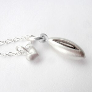 May include: A silver necklace with two charms: a small heart and a larger, elongated oval shape. The necklace is made of a delicate chain.