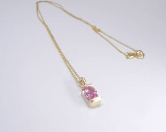 May include: A delicate gold chain necklace with a small pendant featuring a pink oval gemstone set in a gold frame.