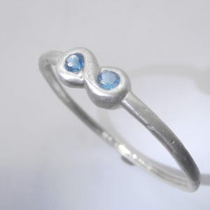 May include: A silver ring featuring two blue gemstones set in a distinctive infinity design.