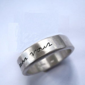 May include: A silver band ring with the inscription "tam vous" engraved on the outside of the band.