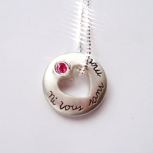 May include: Silver necklace with a heart-shaped pendant that says "Je t'aime" and "Ti amo" in cursive. The pendant has a small red gemstone in the center.