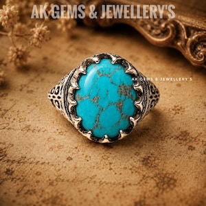 May include: A silver ring featuring a large, oval-shaped turquoise stone with brown matrix veining. The metal band has an intricate, dark-oxidized filigree pattern. The text AK GEMS & JEWELLERY'S is visible at the top and center of the image.