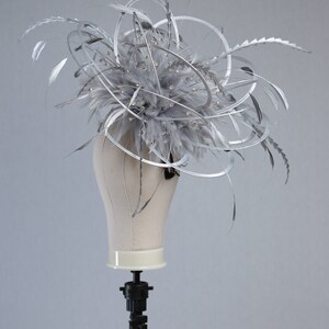 May include: A silver headpiece with feathers, metallic swirls, and sparkling embellishments. The headpiece is displayed on a mannequin head. This elegant accessory is suitable for special occasions.
