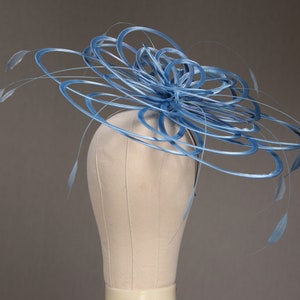 May include: A light blue fascinator hat with a circular design and delicate feather accents. The hat is displayed on a mannequin head, showcasing its intricate details and elegant style. Perfect for special occasions.