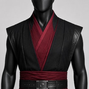 May include: A sleeveless black vest featuring a deep V-neckline with layered dark red fabric underneath. The garment includes a wide, textured dark red sash at the waist, secured by a black belt with a central square buckle featuring circular details.
