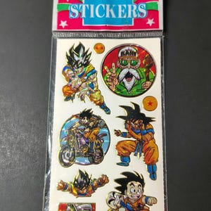 May include: A sheet of holographic Dragon Ball stickers in clear plastic packaging with a header reading STICKERS. The sheet features various characters including Goku in different poses, Master Roshi, and Piccolo, along with two orange star balls.