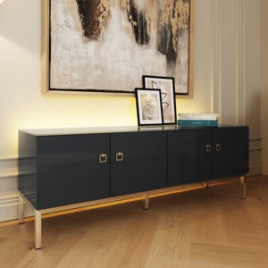 May include: A dark grey sideboard with four doors, each featuring a square silver handle. The unit has a smooth top surface and is supported by four silver metal legs. Two framed line art prints and a stack of books sit on the sideboard top.