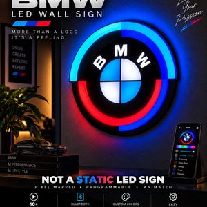May include: A circular BMW LED wall sign featuring a black background with white lettering and a central emblem illuminated in blue and red. The sign is programmable and animated, controlled via a smartphone app, and displays the text BMW LED WALL SIGN, MORE THAN A LOGO IT'S A FEELING, and NOT A STATIC LED SIGN.