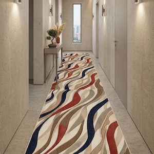 May include: A long runner rug featuring a wavy, abstract pattern in shades of cream, beige, deep red, and navy blue. The rug is positioned in a narrow hallway with light-colored walls, recessed wall lighting, and a slim console table.
