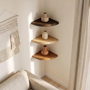 Peut inclure: Trois étagères d'angle superposées en bois dans des tons variés de brun foncé, beige clair et chêne moyen. Chaque étagère supporte un vase en céramique dans une teinte neutre assortie, installées dans l'angle d'une pièce aux murs clairs.