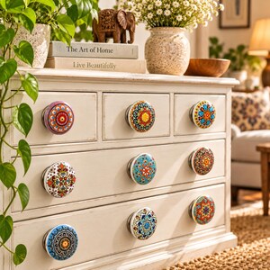 Peut inclure: Une commode en bois blanc dot&eacute;e de huit boutons de tiroir ronds, chacun orn&eacute; d'un motif mandala unique, color&eacute; et complexe dans des tons de bleu, orange, rouge, jaune et vert, sur une finition blanc cass&eacute; l&eacute;g&egrave;rement vieillie.